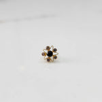 A gold nose pin shaped like a star with a black center stone and pale champagne accent stones