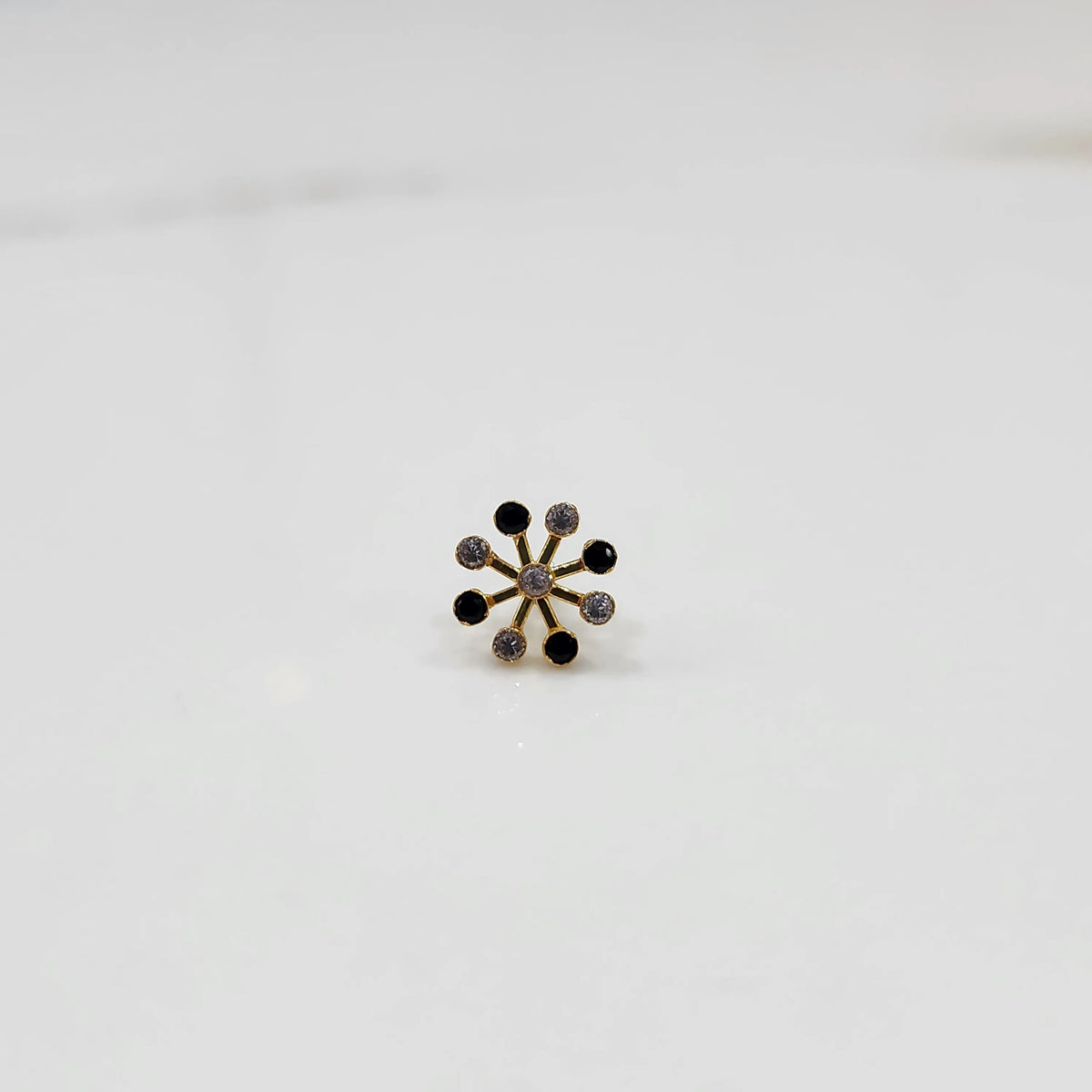Product shot of a gold nose stud with alternating black onyx and diamond stones