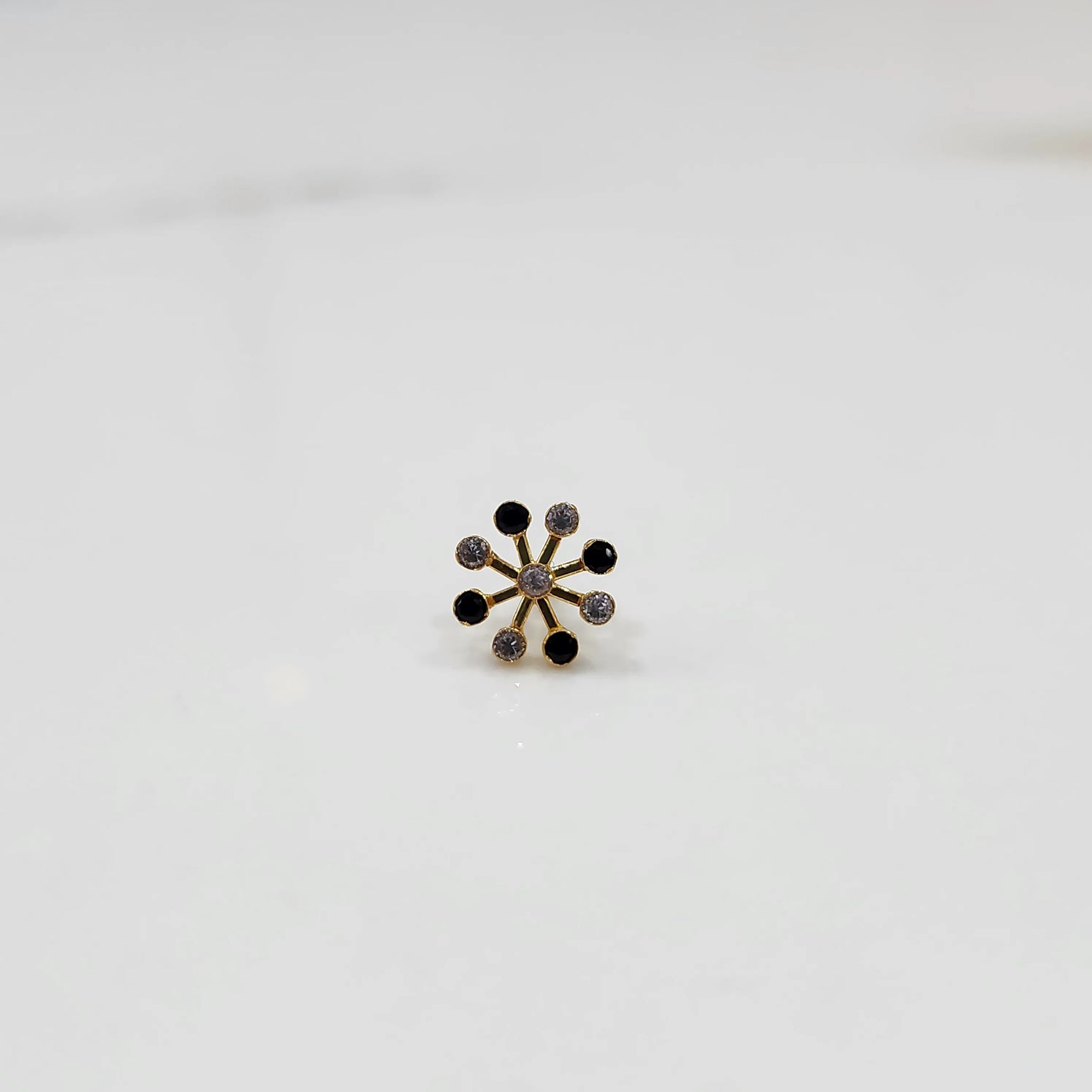Product shot of a gold nose stud with alternating black onyx and diamond stones