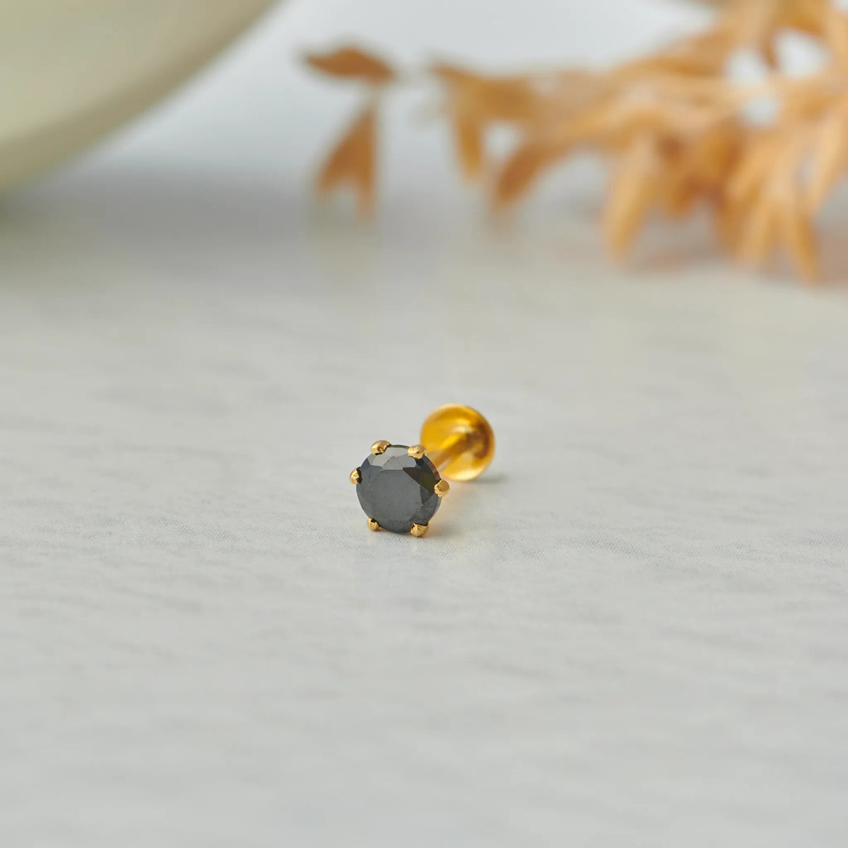 Close up of single black stone gold nose pin on white surface