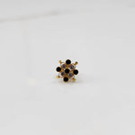 A gold nose pin shaped like a flower, set with alternating black and clear crystal stones.