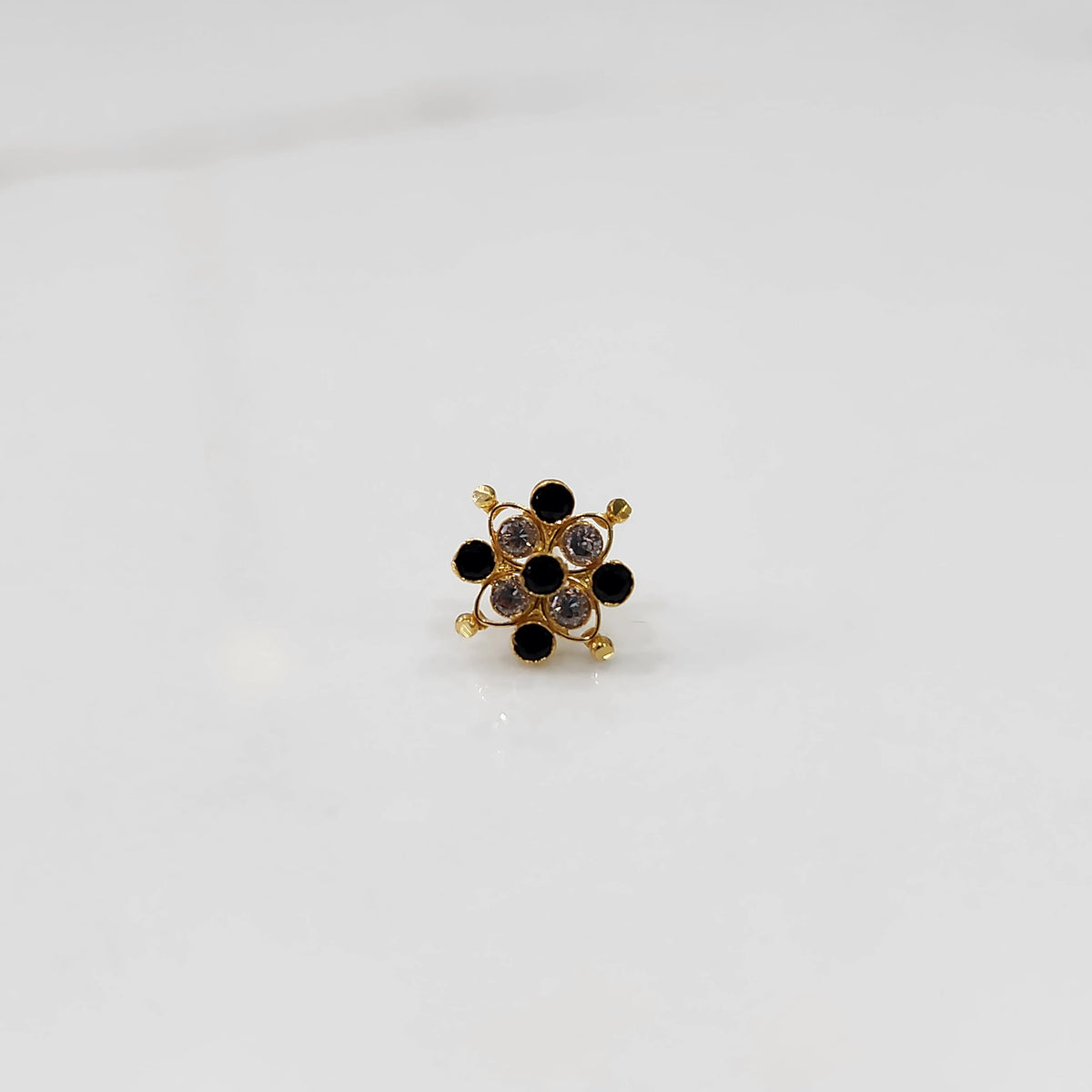 A gold nose pin shaped like a flower, set with alternating black and clear crystal stones.