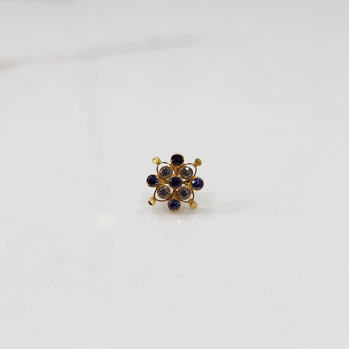 A gold nose pin shaped like a flower, set with blue sapphire-toned and clear crystal stones