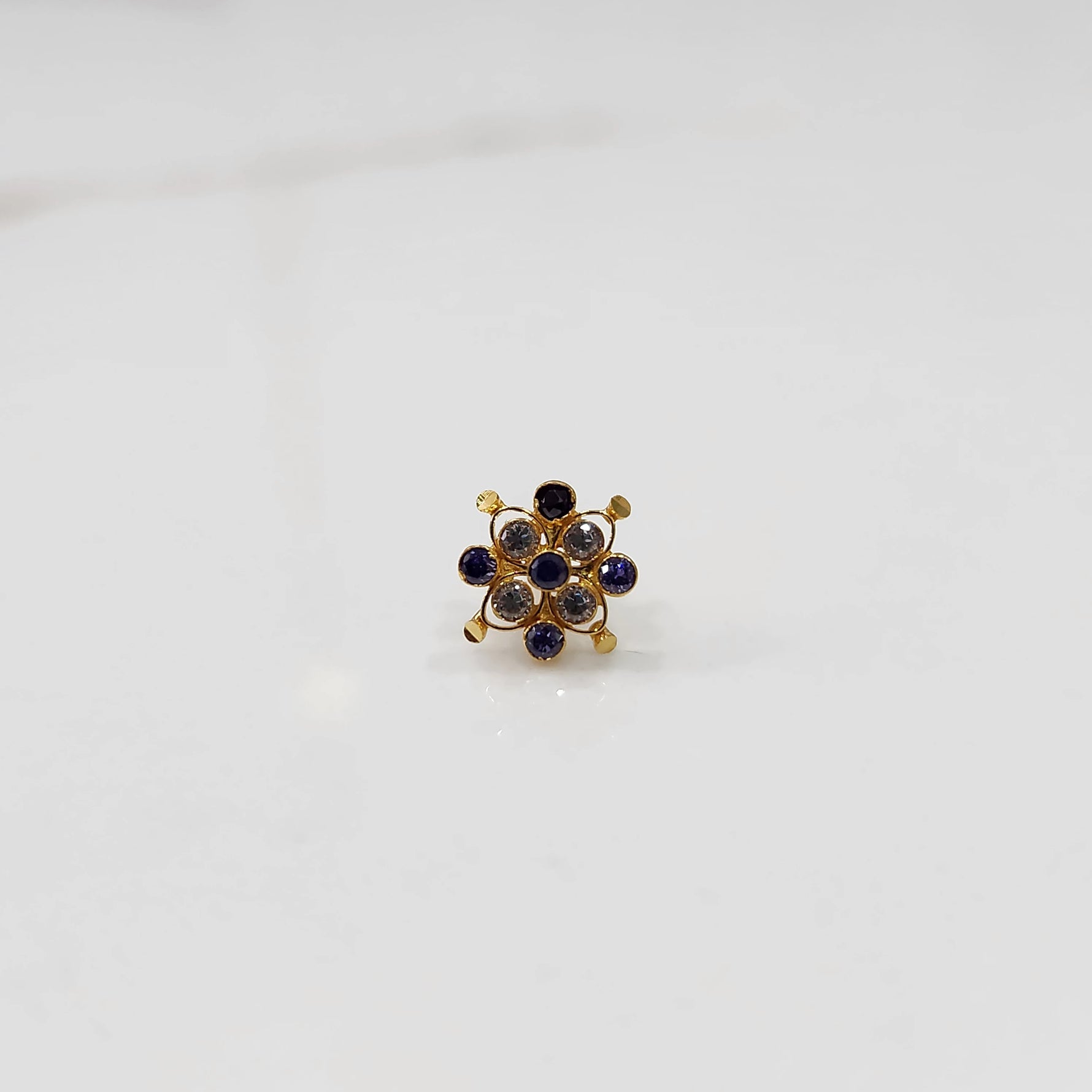 A gold nose pin shaped like a flower, set with blue sapphire-toned and clear crystal stones