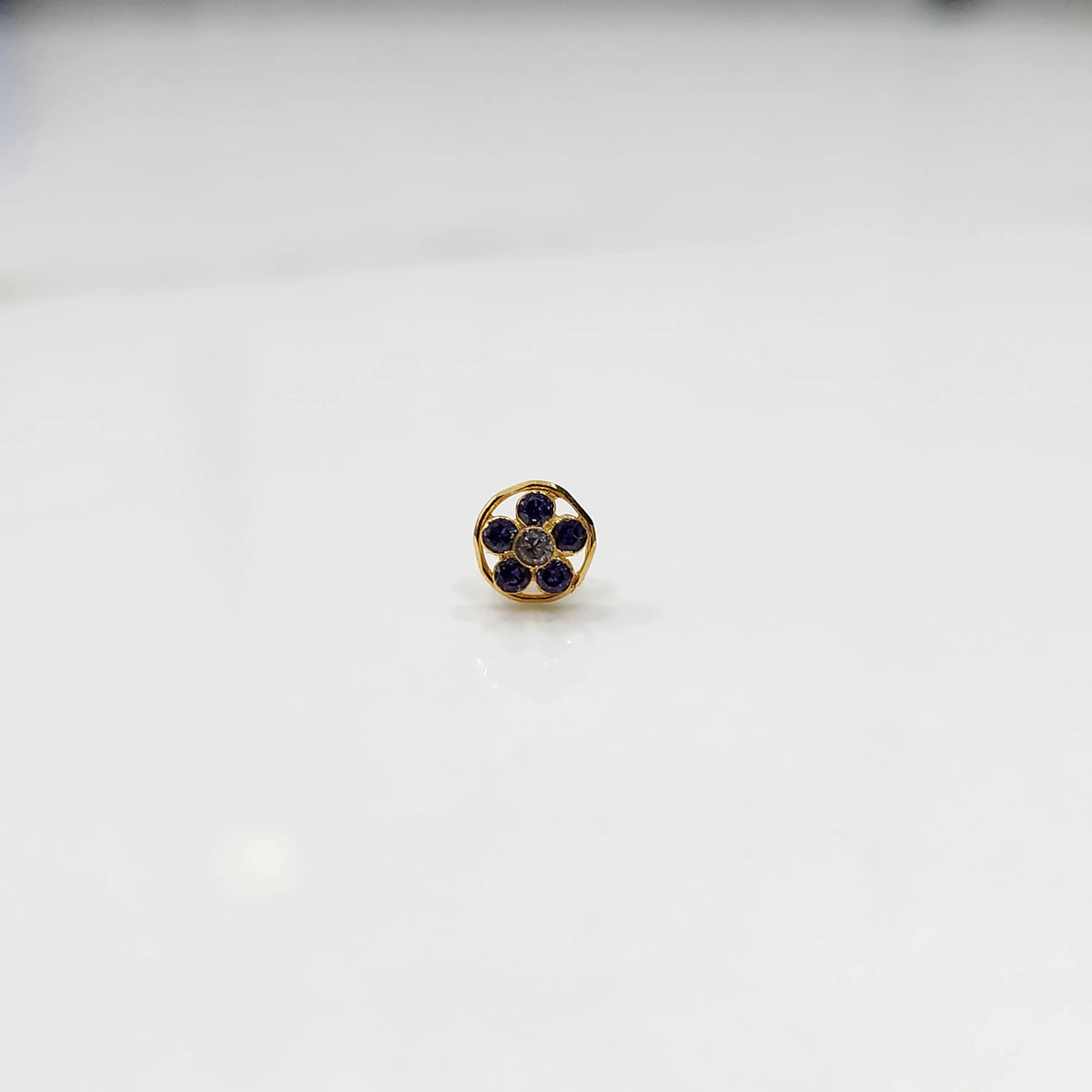 Product shot of a round gold nose stud with blue sapphire gemstone flower cluster