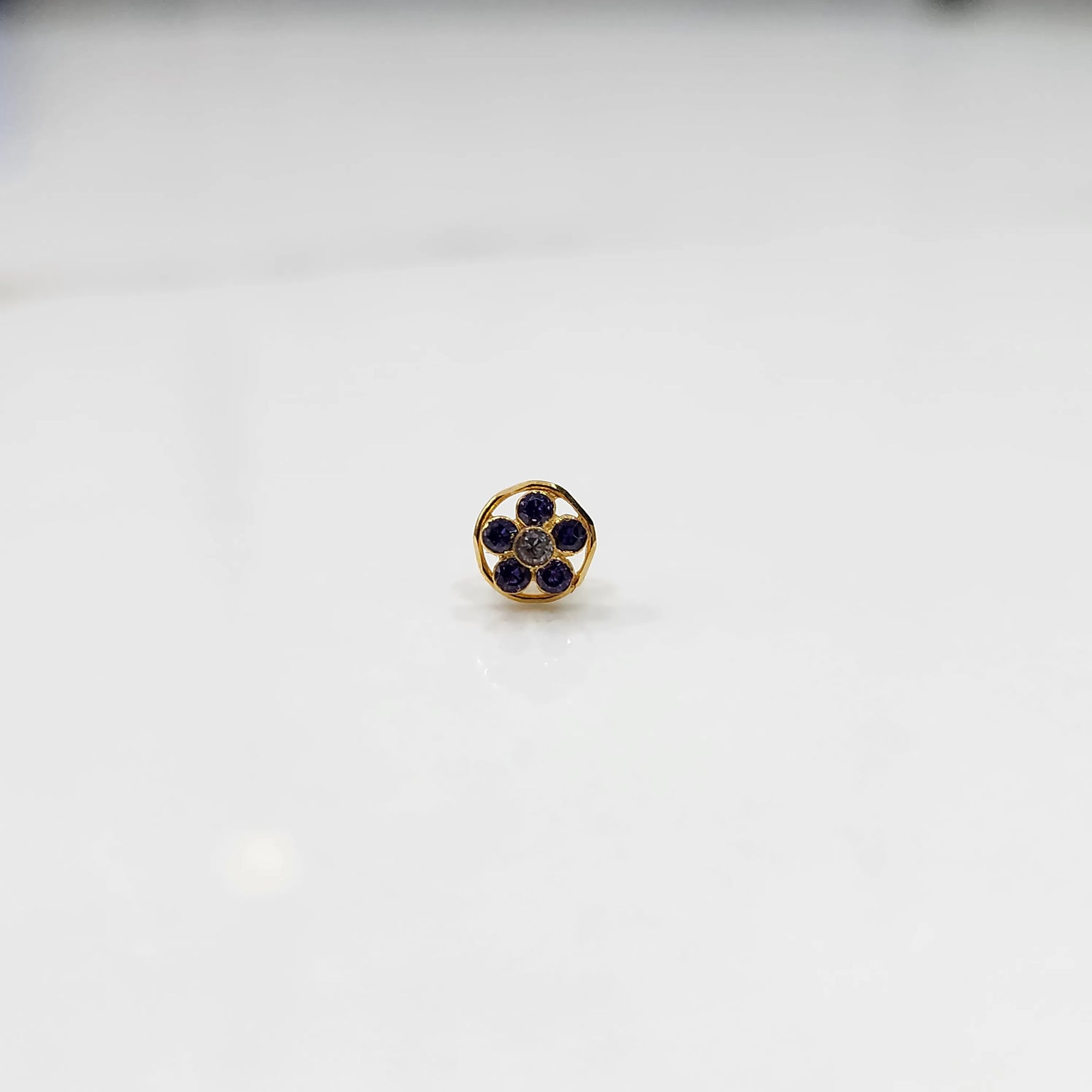Product shot of a round gold nose stud with blue sapphire gemstone flower cluster