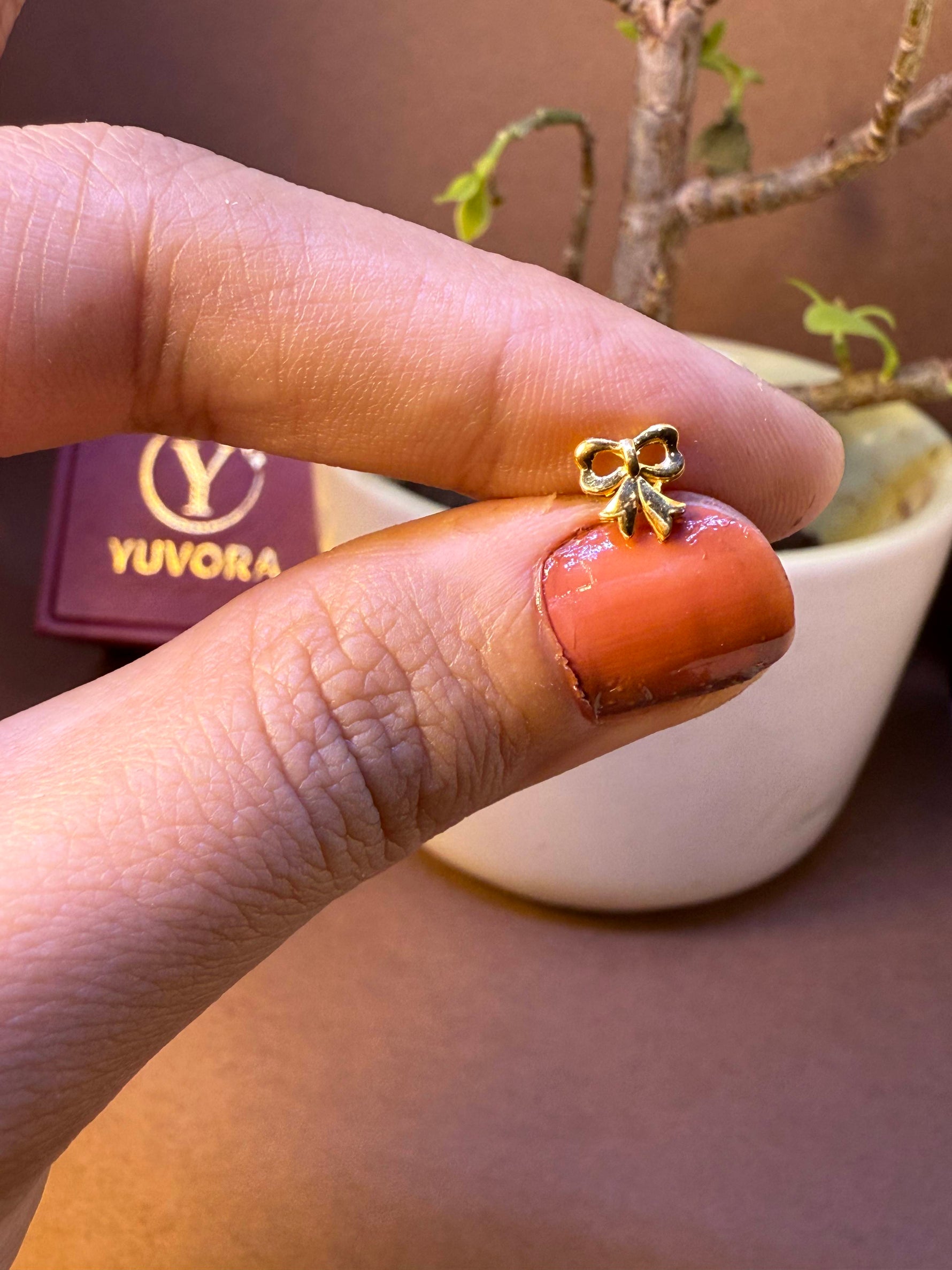 Bow-shaped gold nose pin, held between fingertips