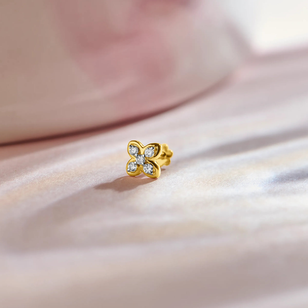 Flower nose pin gold with cute four-petal floral design featuring sparkling stones set in a polished gold base on a soft pink satin background