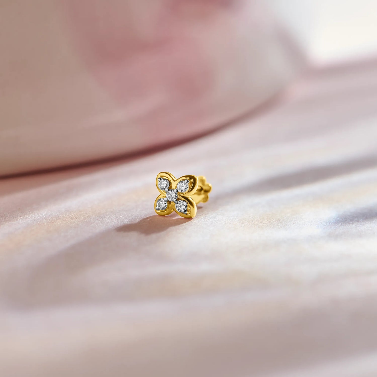 Flower nose pin gold with cute four-petal floral design featuring sparkling stones set in a polished gold base on a soft pink satin background