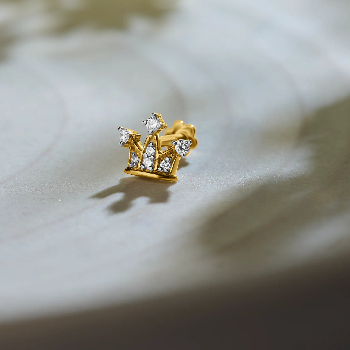 Trending gold nose pin with crown-inspired diamond design on textured background