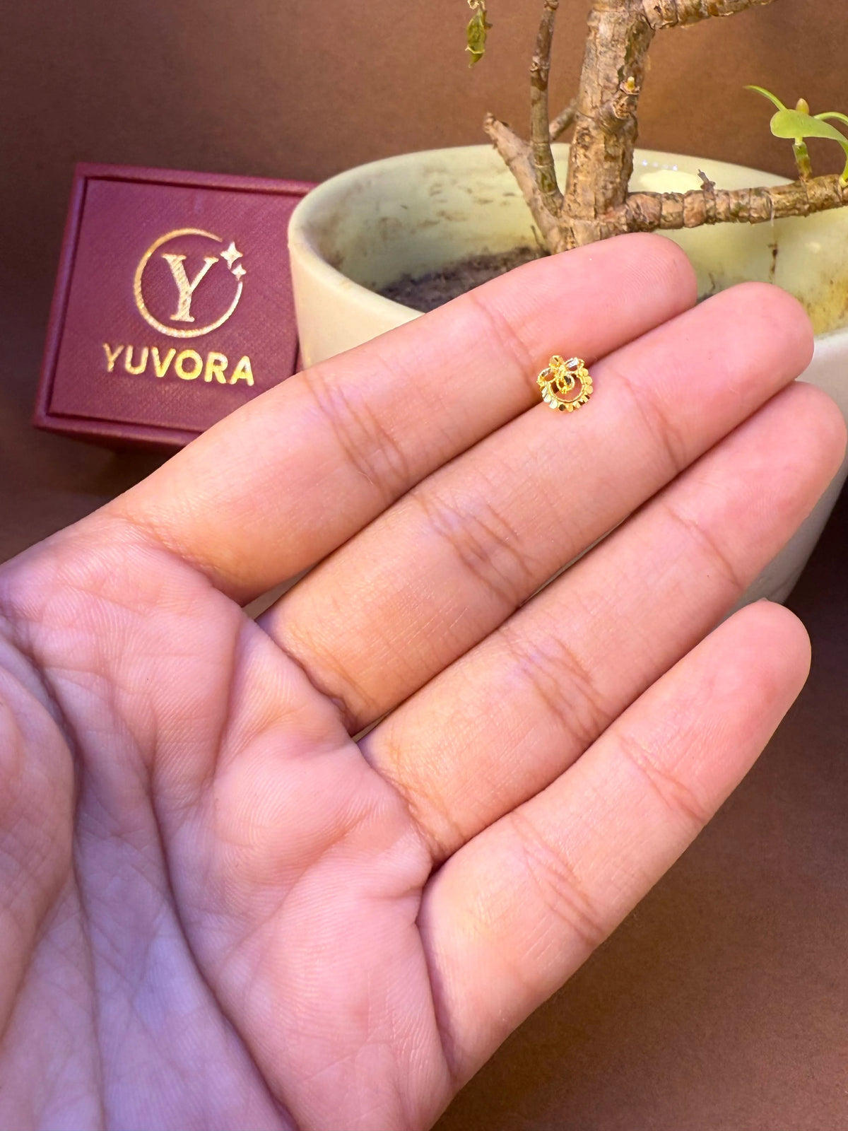 Round gold nose pin with scalloped crown-edge design and open center, held in hand