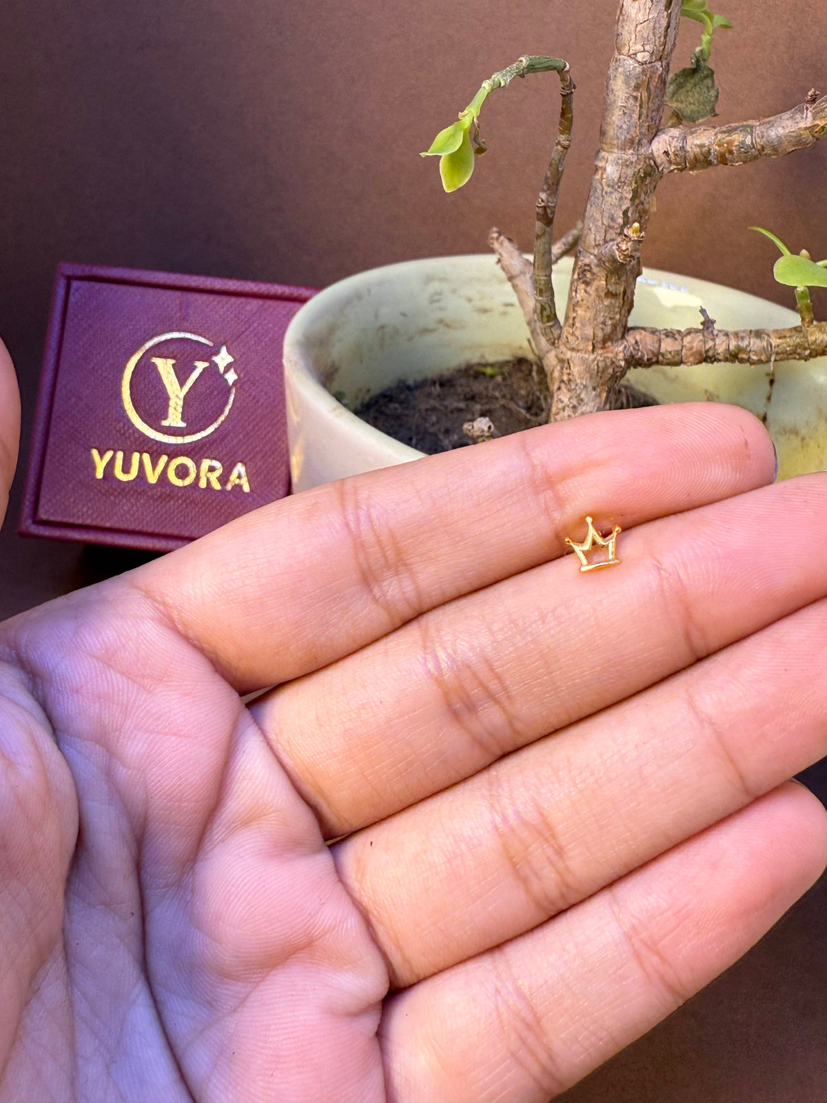 Crown-shaped gold nose pin, small and delicate, held in hand