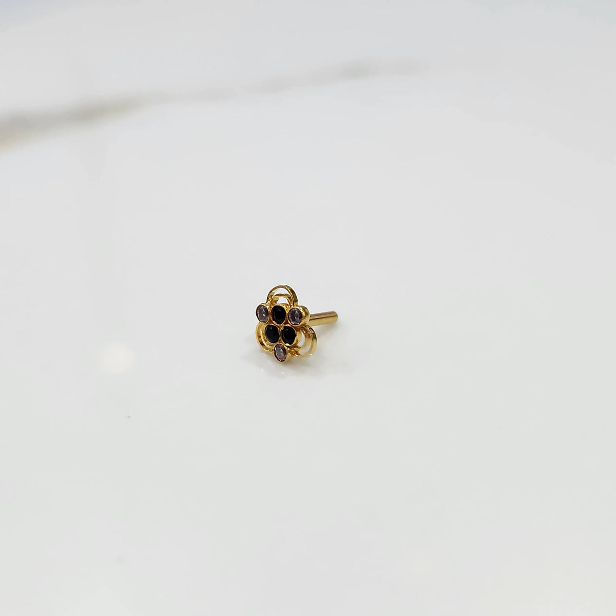 Side tilted view of the stone gold nose pin on a white surface focusing on depth and setting height