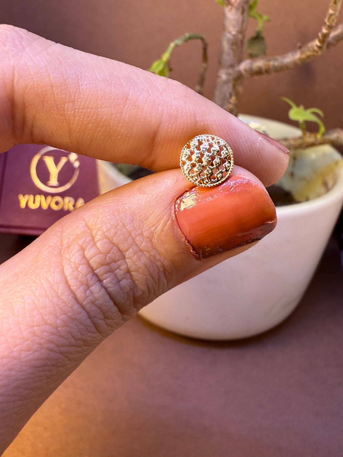 Round gold nose pin with fine mesh dome texture, held between fingertips