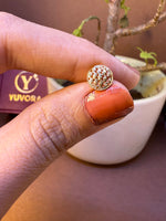 Round gold nose pin with fine mesh dome texture, held between fingertips