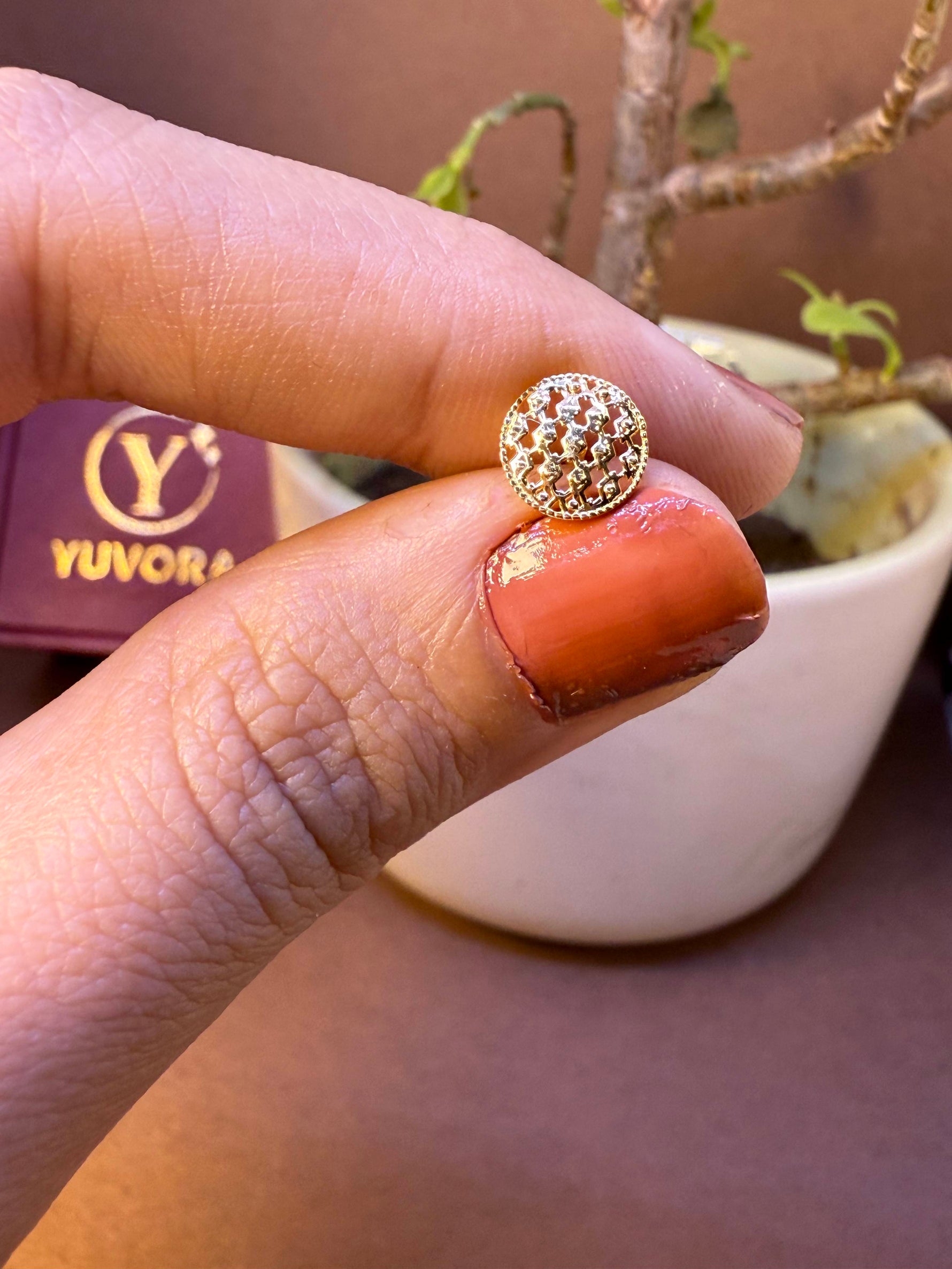 Round gold nose pin with fine mesh dome texture, held between fingertips