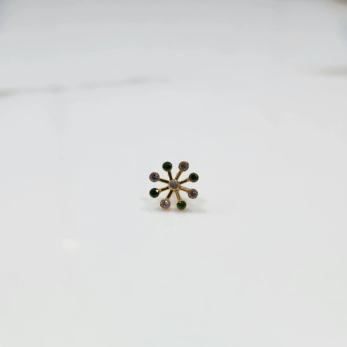 Product shot of a gold nose stud with alternating emerald and diamond stones