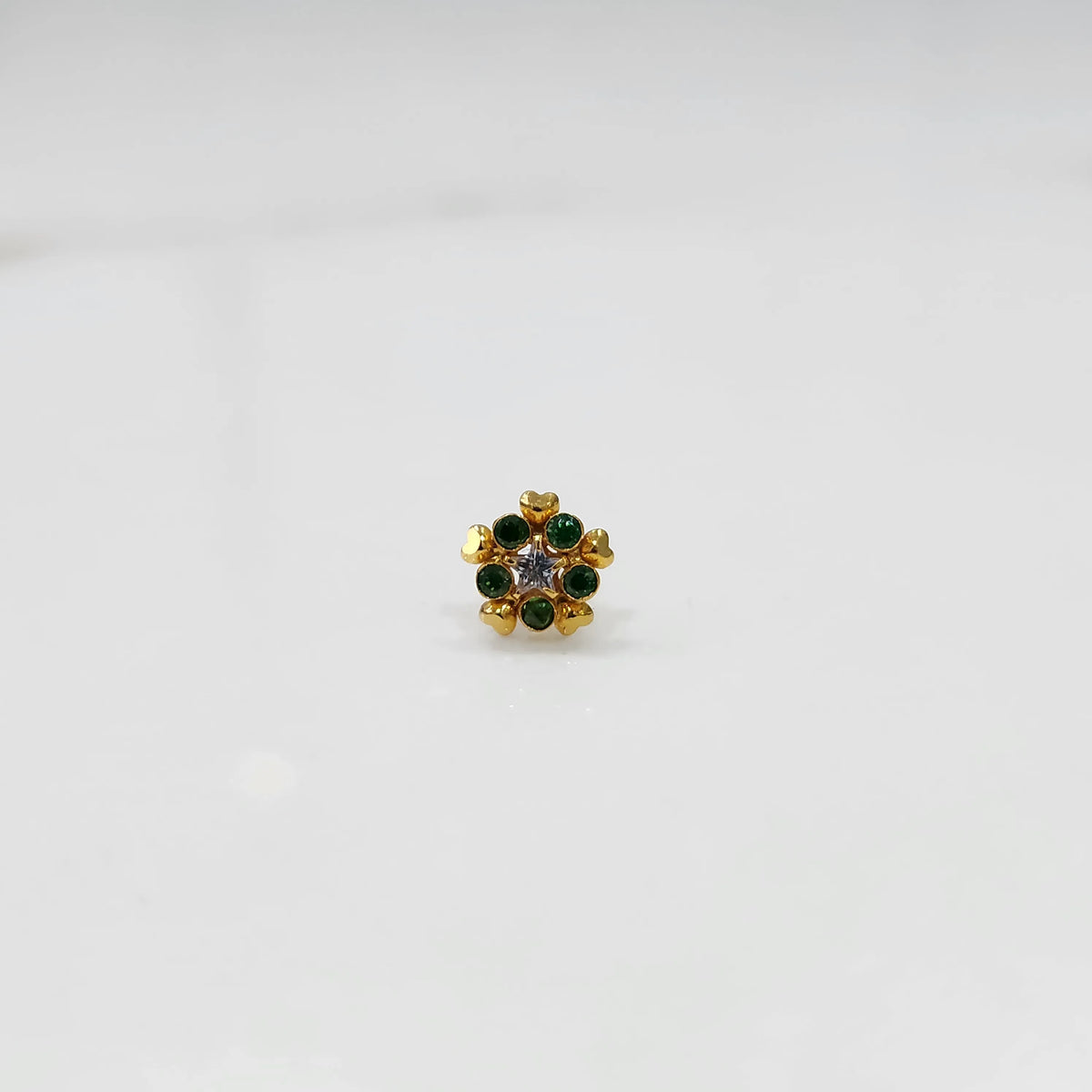 Product shot of a gold nose stud with emerald green gemstone flower and heart petal design