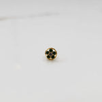 Product shot of a round gold nose stud with emerald green gemstone flower cluster