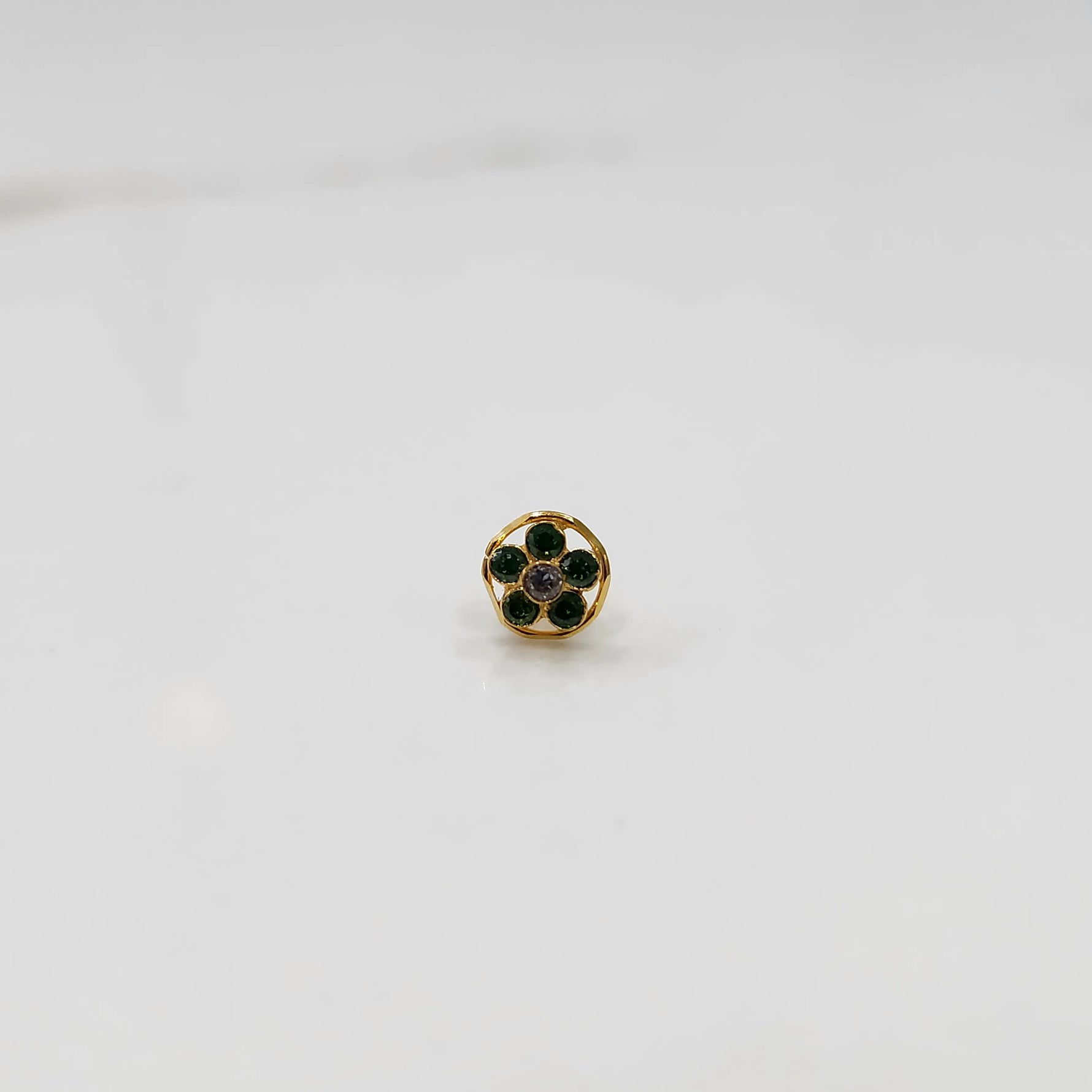 Product shot of a round gold nose stud with emerald green gemstone flower cluster