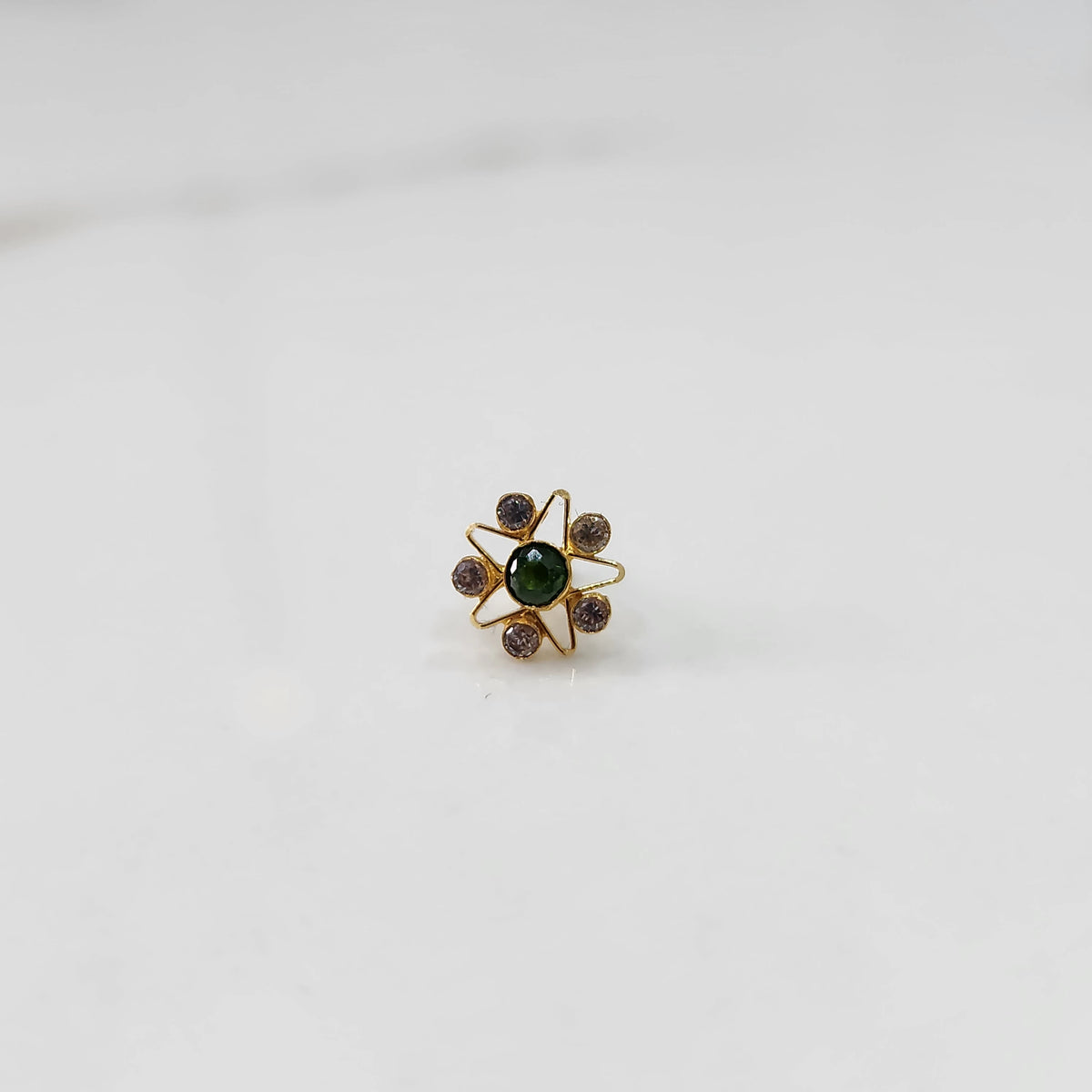 A gold nose pin shaped like a star with a green center stone and light purple accent stones