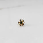 A gold nose pin shaped like a star with a green center stone and light purple accent stones