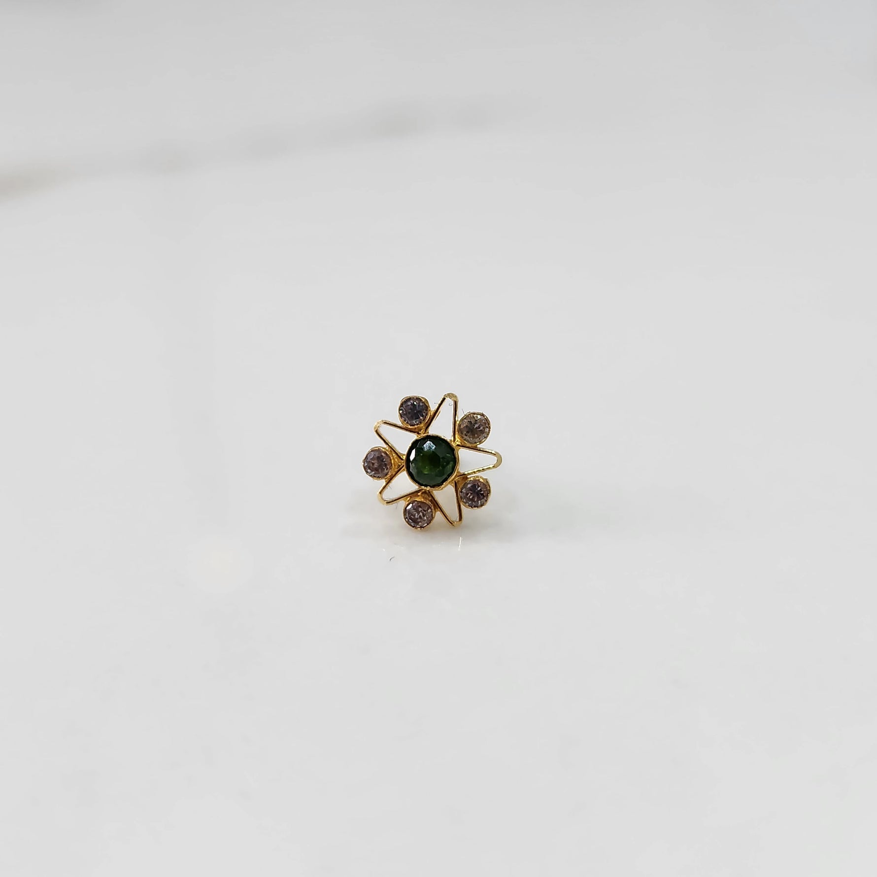 A gold nose pin shaped like a star with a green center stone and light purple accent stones