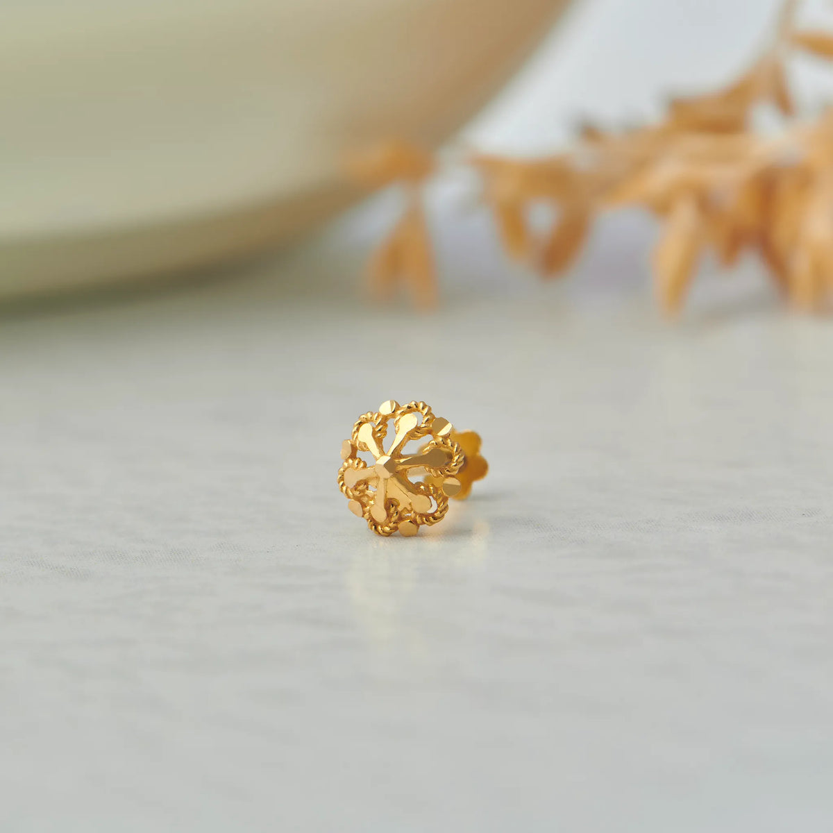 Close up of floral gold nose pin placed on a light surface highlighting intricate openwork design