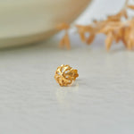 Close up of floral gold nose pin placed on a light surface highlighting intricate openwork design