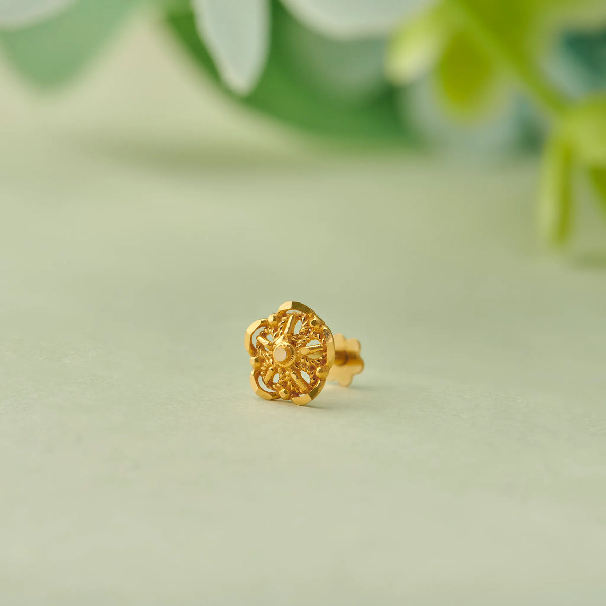 Close up of floral 18K gold nose pin placed on a soft green background highlighting detailed craftsmanship