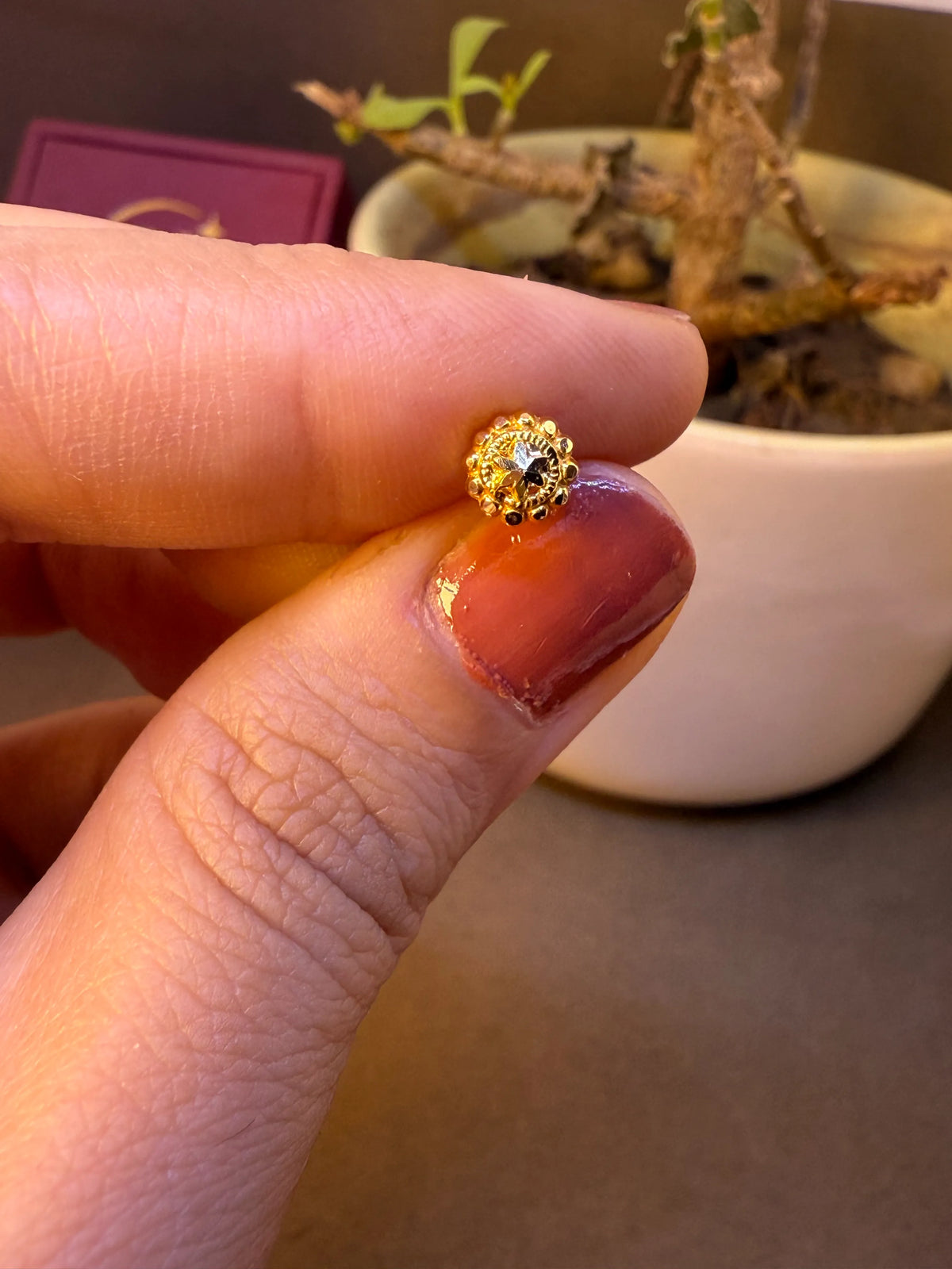 Close-up of round beaded gold nose pin with white stone center, held between fingertips