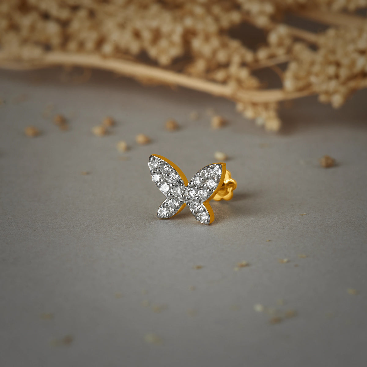 Stone Gold Nose Pin with butterfly design studded with sparkling stones on a soft textured background