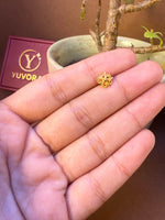 Four-petal gold nose pin with curled wire design held in hand, Yuvora jewelry box in background