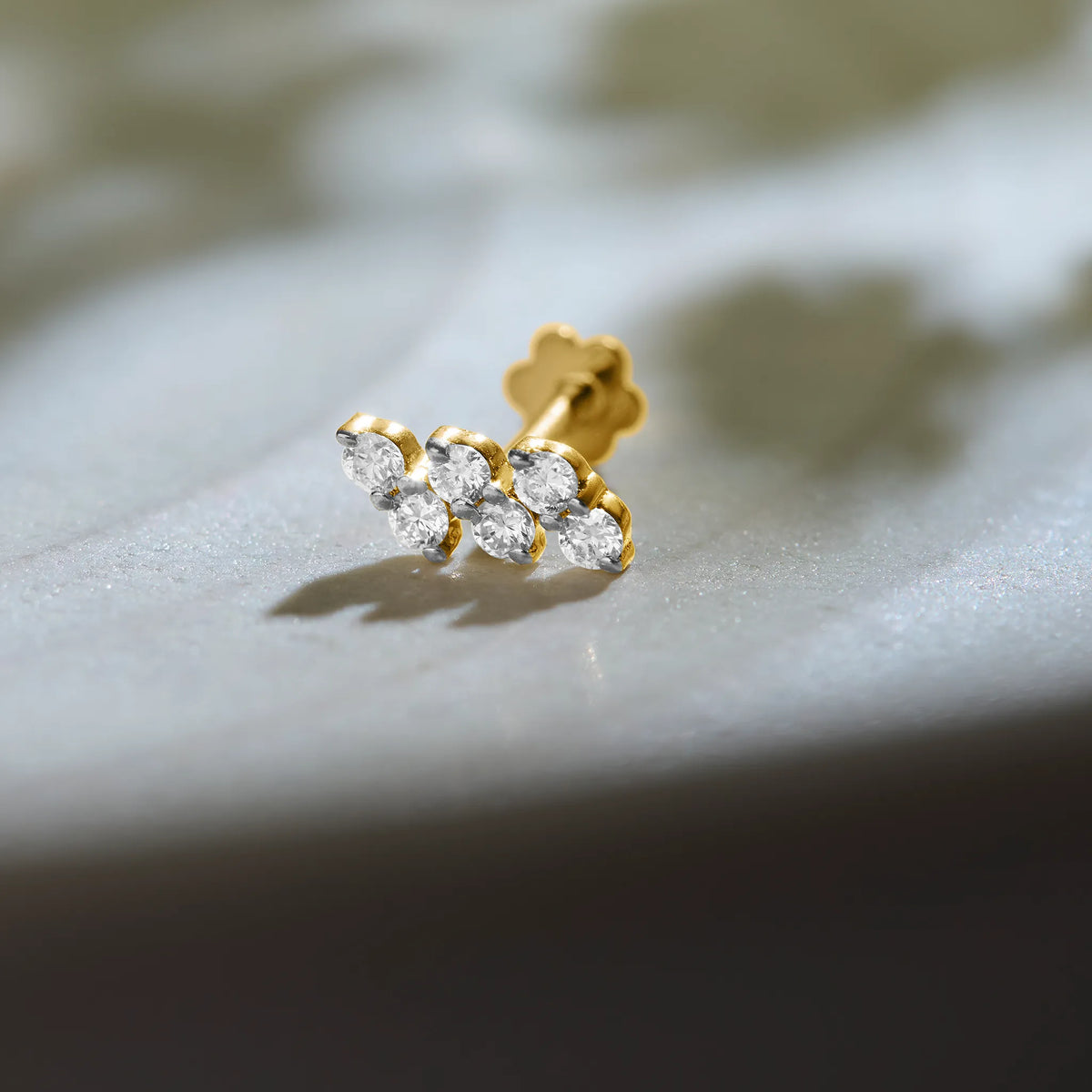 Gold diamond nose pin with triple stone design on soft background
