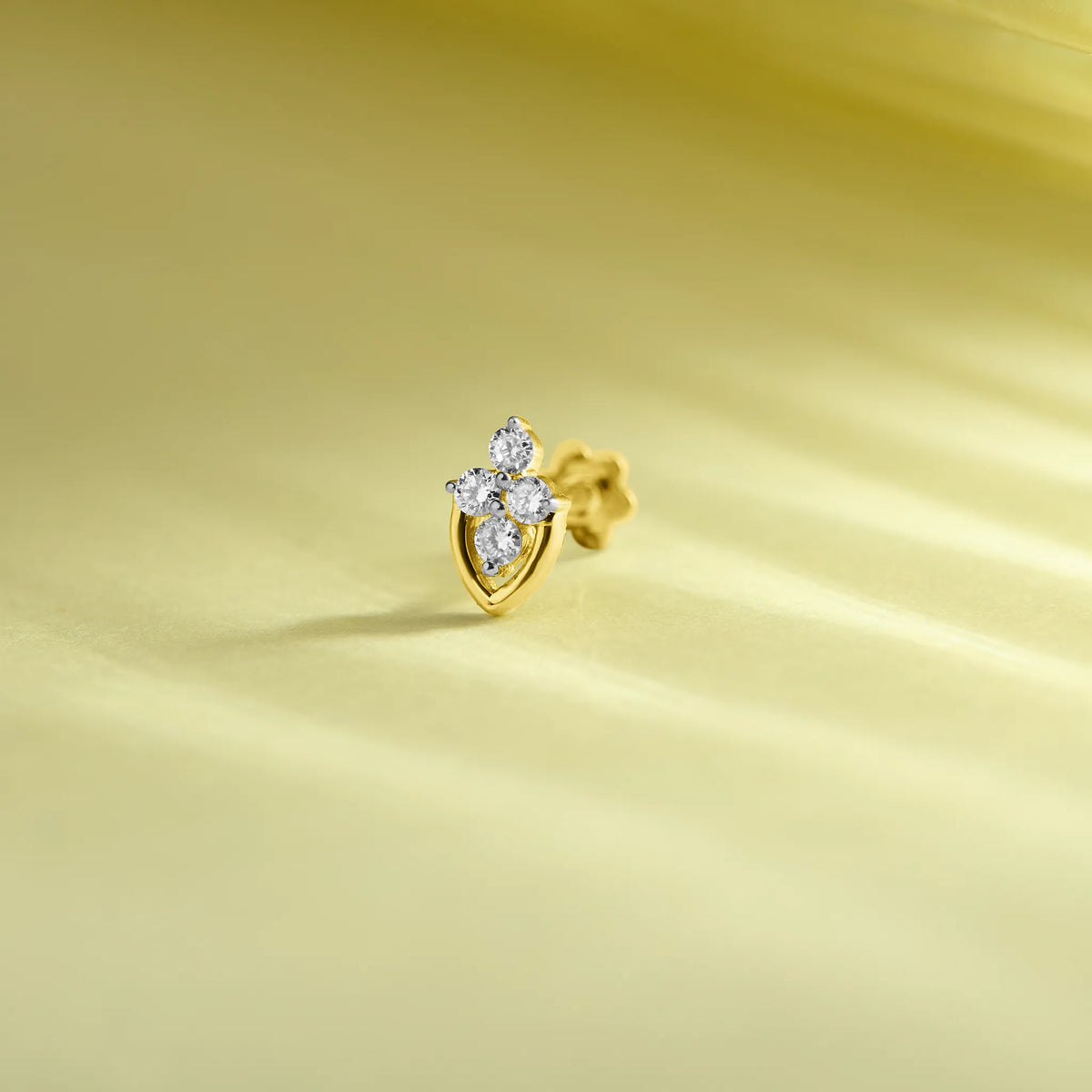 Gold leaf-shaped diamond nose pin design on soft pastel background