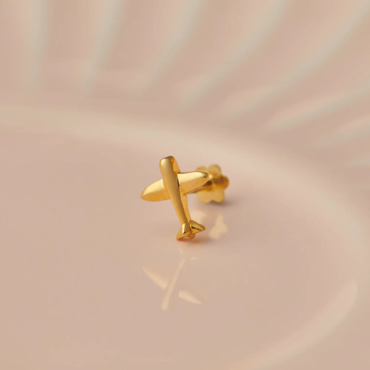 Gold airplane-shaped nose stud on beige background