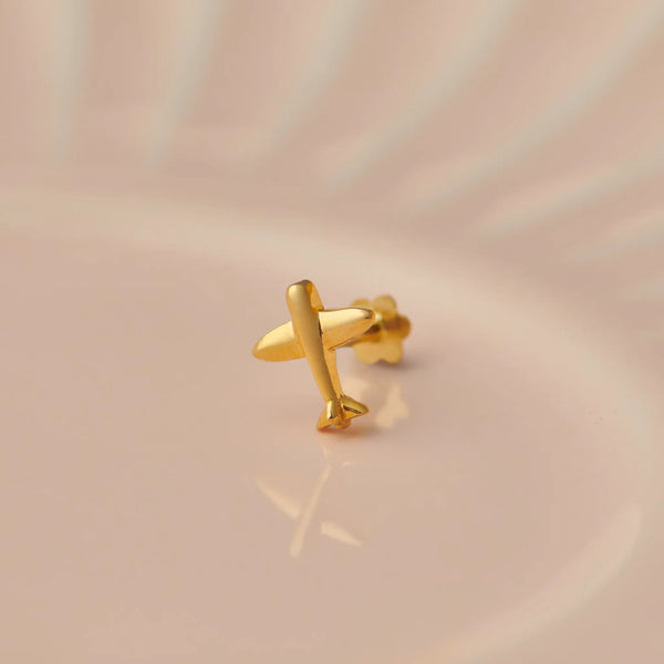 Gold airplane-shaped nose stud on beige background