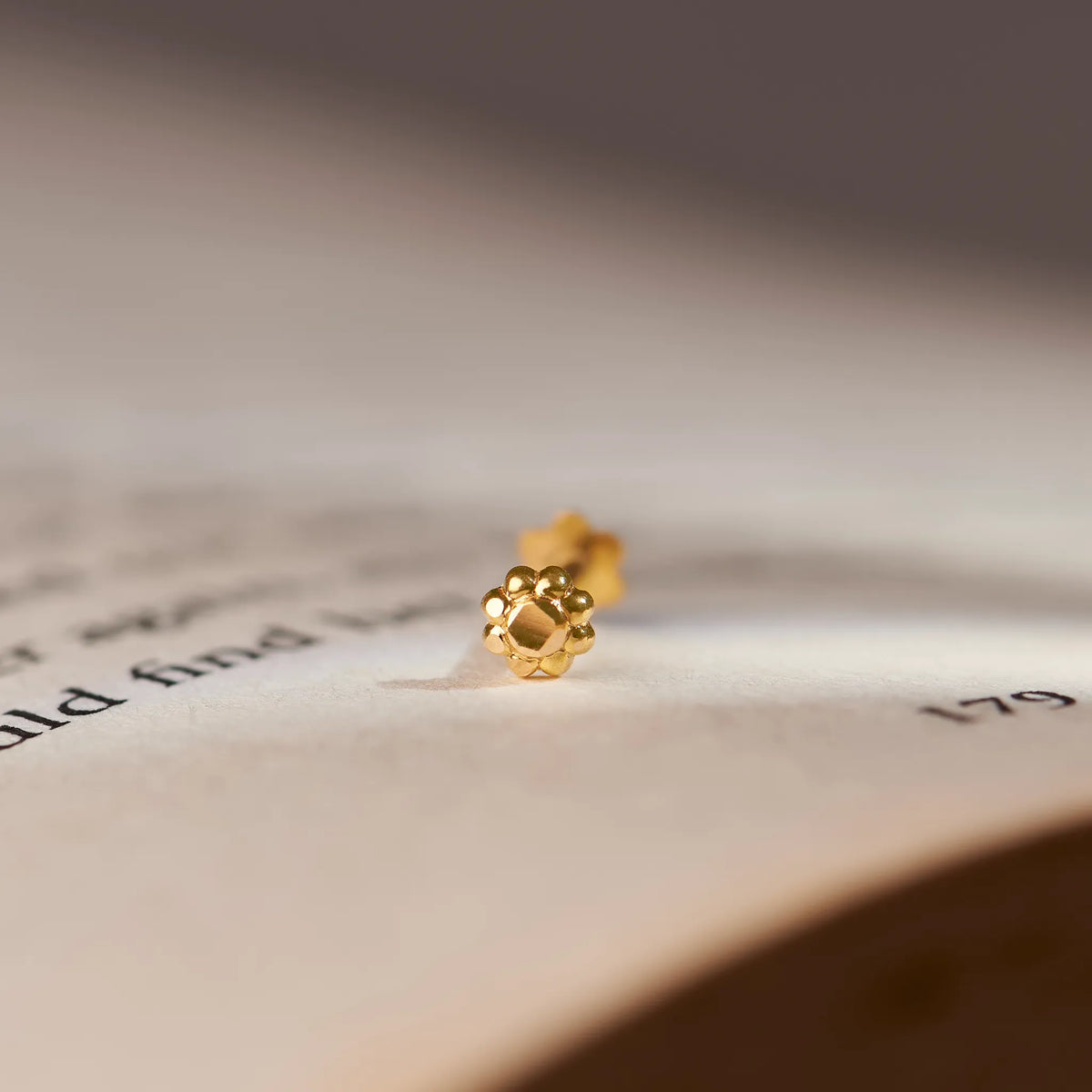 Gold dotted-petal flower stud earring, close-up