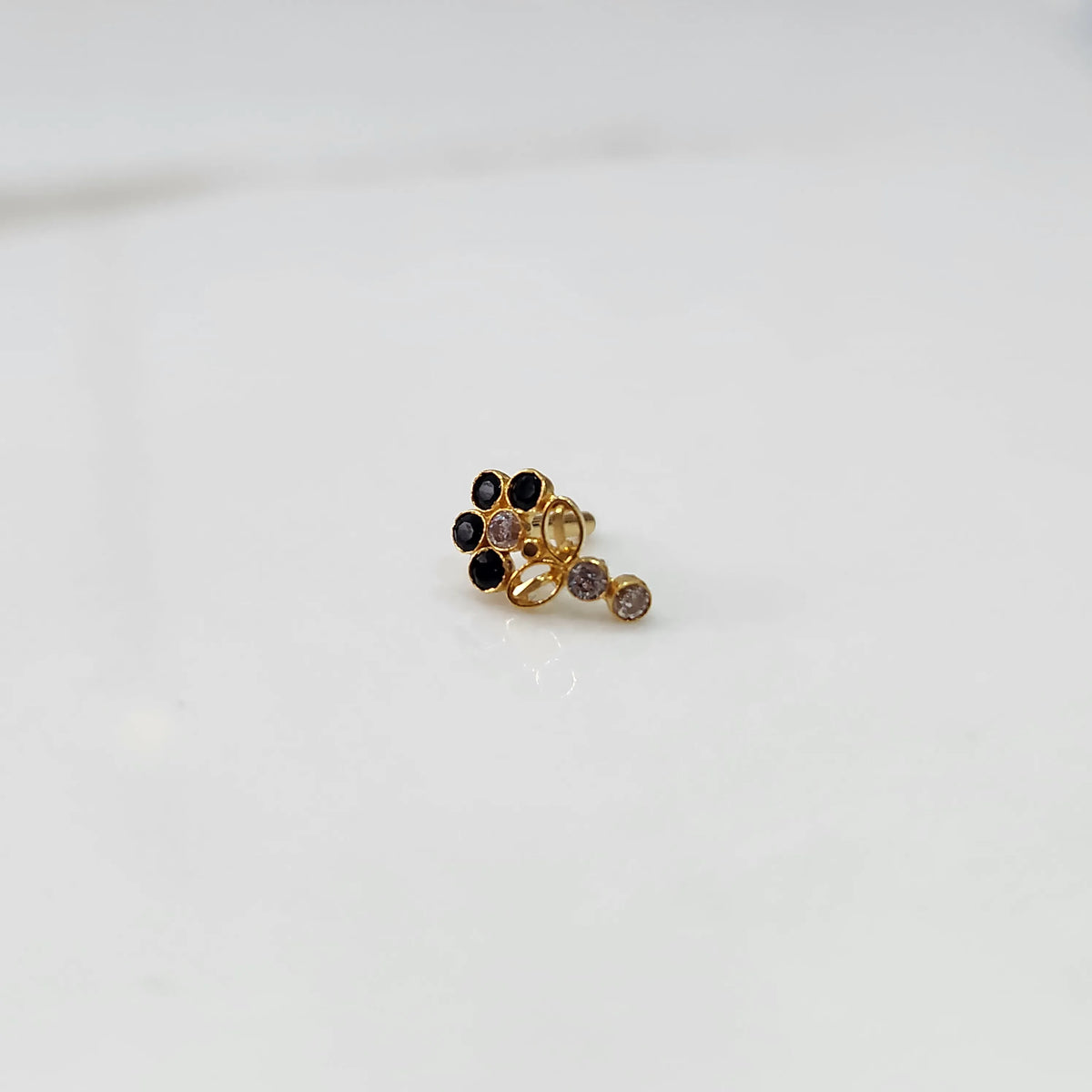 Gold nose pin with black gemstone cluster and clear drop-style stone accent on white background