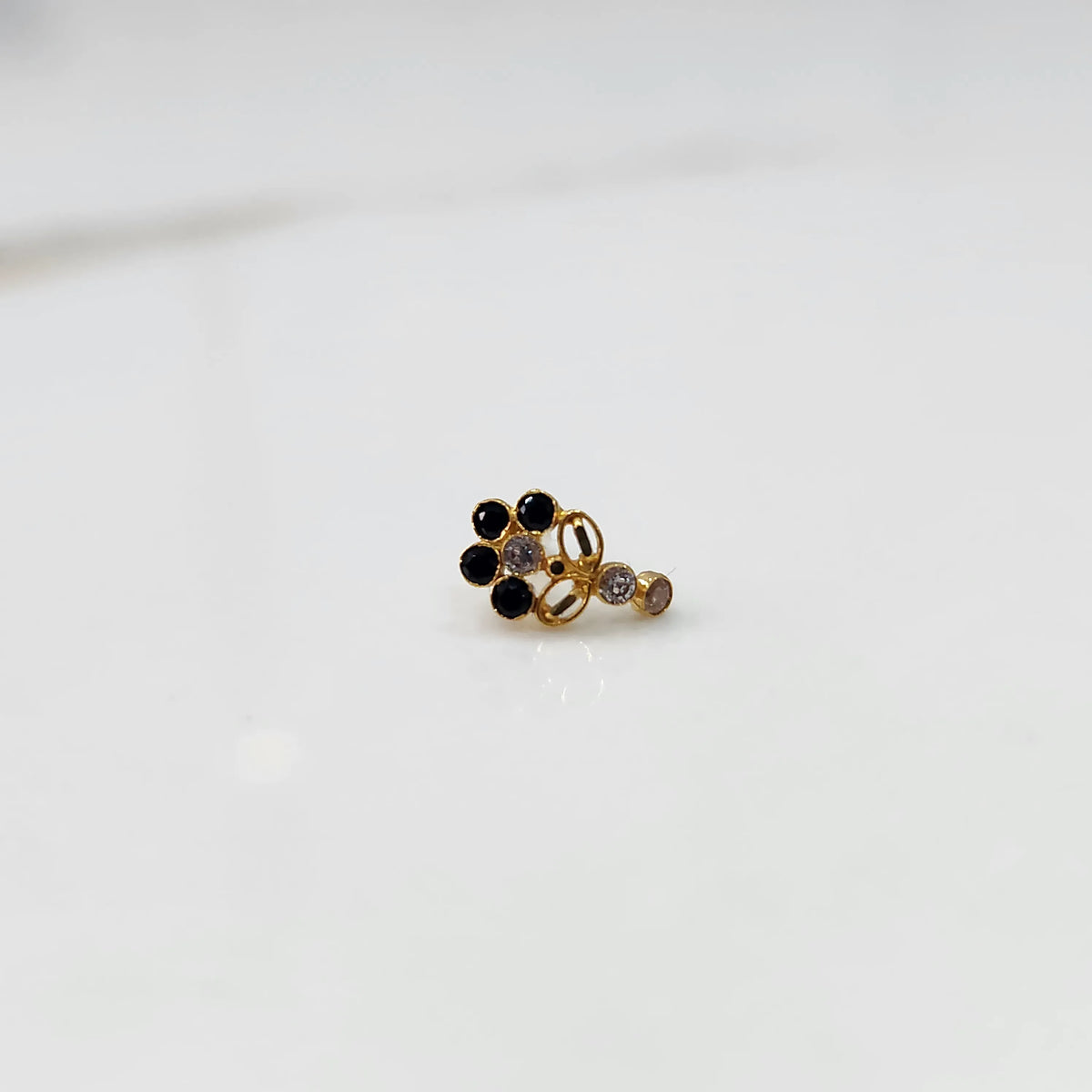 Front view of gold nose pin with black gemstone cluster and clear drop-style stone accent on white background