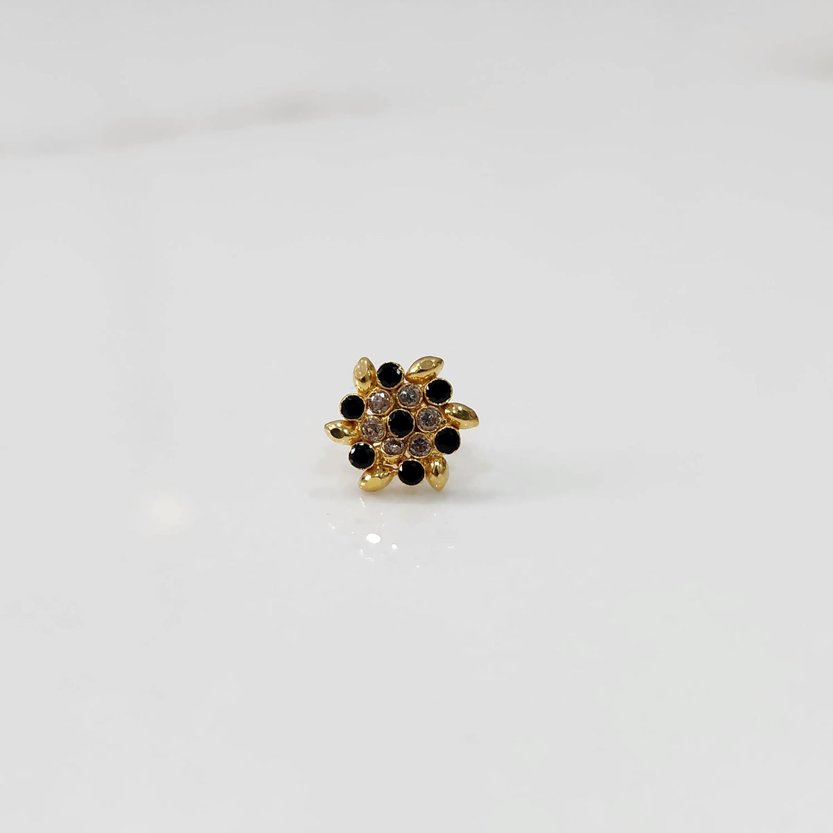 Front view of gold statement ring with black and clear gemstones in leaf-patterned cluster design