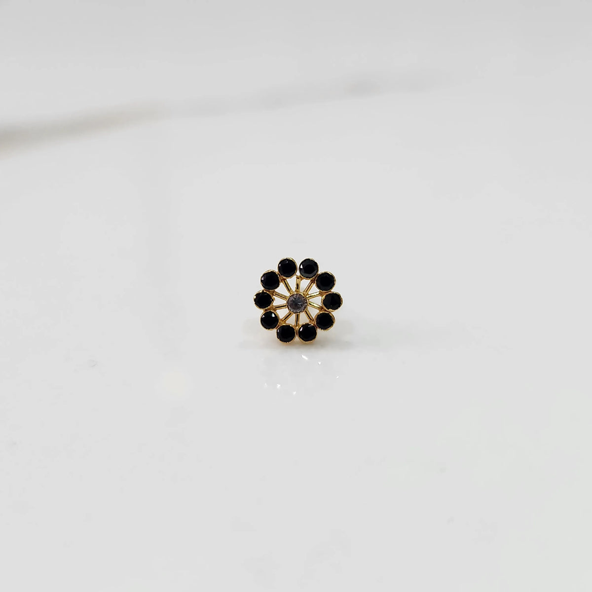 Front view of large gold nose pin with black gemstone flower design on white background