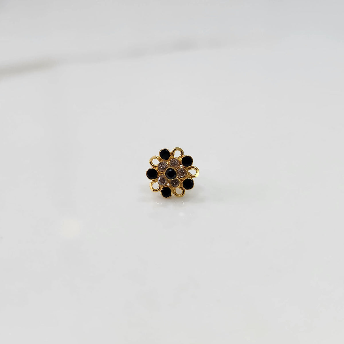 Front view of gold nose pin with black gemstone mandala design on white background