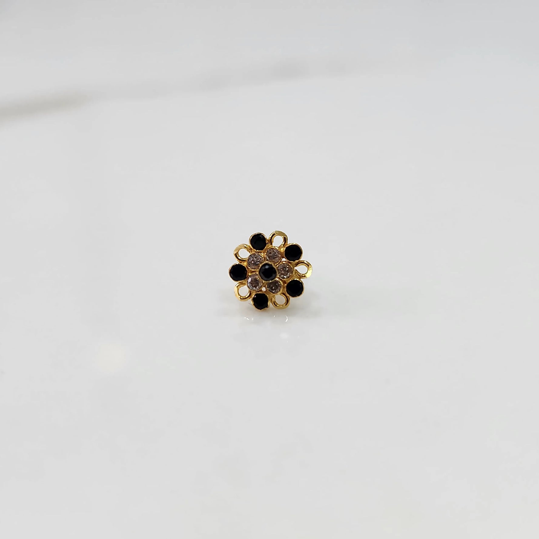 Front view of gold nose pin with black gemstone mandala design on white background