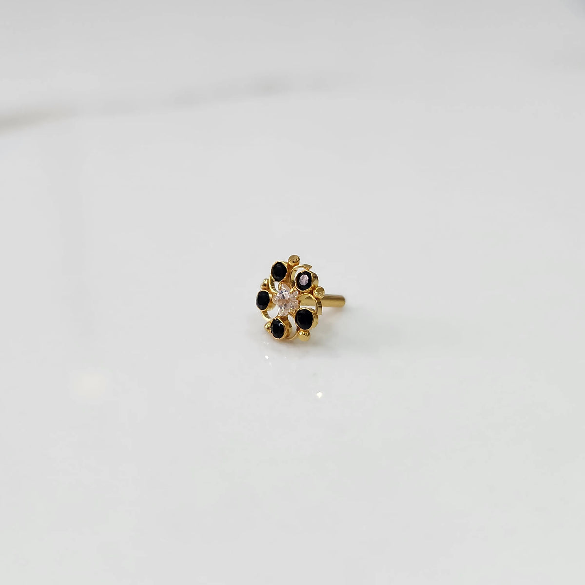 Gold nose pin with black gemstone petals and clear center stone on white background