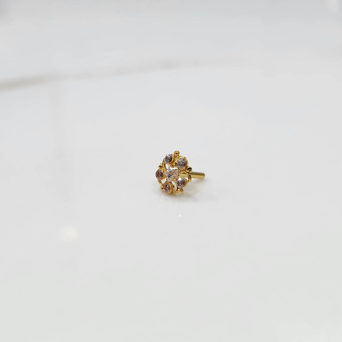 Front view of gold nose pin with black gemstone petals and clear center stone on white background