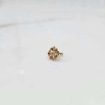 Front view of gold nose pin with black gemstone petals and clear center stone on white background