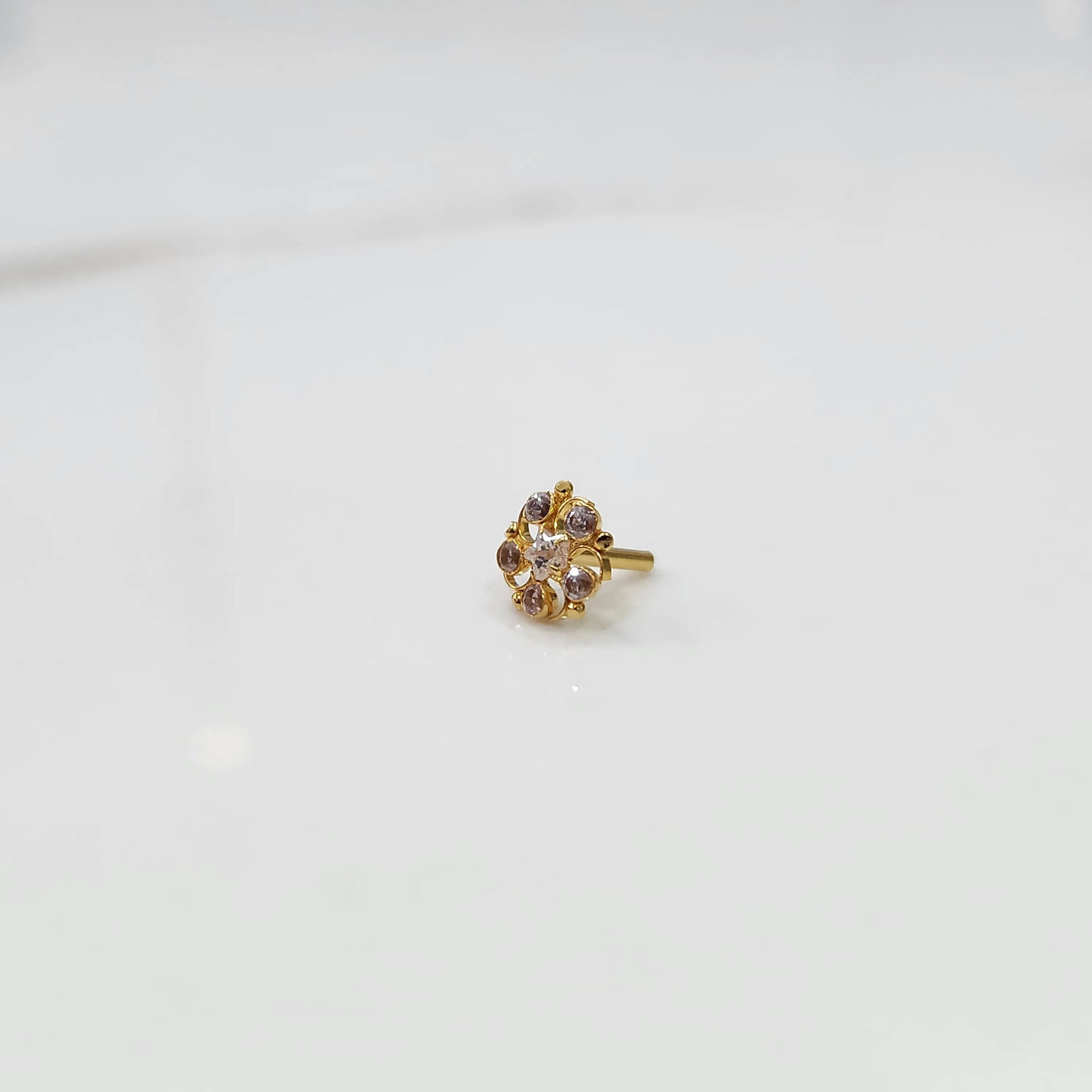 Front view of gold nose pin with black gemstone petals and clear center stone on white background