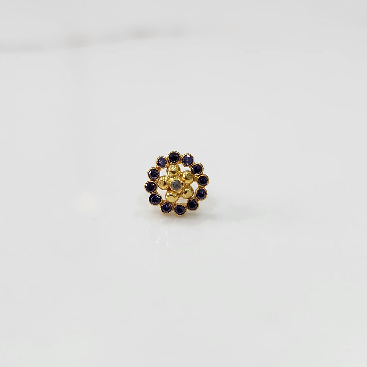 Close-up of flower-shaped gold nose pin with blue gemstone border