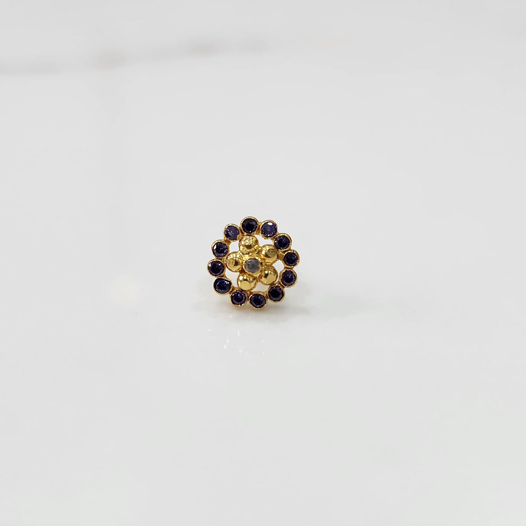 Close-up of flower-shaped gold nose pin with blue gemstone border